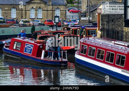 Tourist leisure trip on water (men women, self-drive red hire boat stern, busy marina moorings) - scenic Leeds-Liverpool Canal, Yorkshire, England UK. Stock Photo