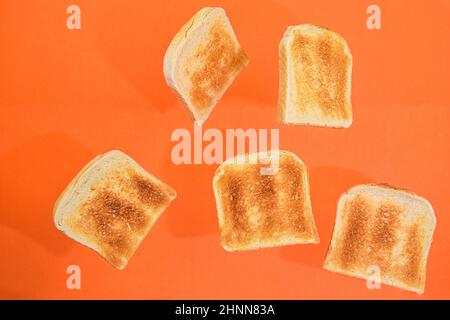 Flying roasted pieces of bread on orange pastel background. Fresh roasted pieces of toasts on orange background. Stock Photo