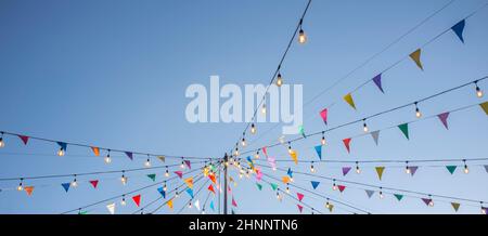 Garland with colorful pennants and light bulbs on pole over blue sky. Long format Stock Photo