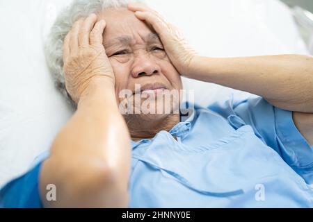Asian senior or elderly old lady woman patient headache while sitting on bed in nursing hospital ward, healthy strong medical concept Stock Photo