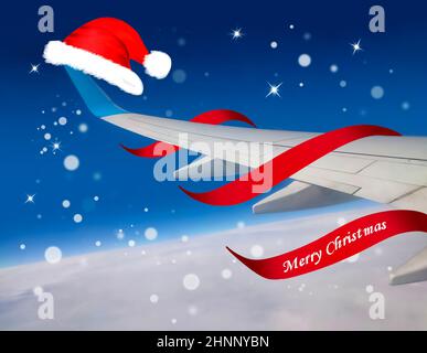 Airplane with red Santa Christmas hat over clouds and blue sky. Stock Photo