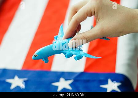 Close up of young woman holding airplane toy in her hand. United States of America flag on the background. Stock Photo