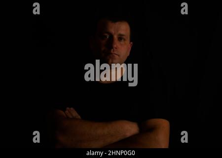 Young man with folded arms in a black T-shirt on a black background. Stock Photo