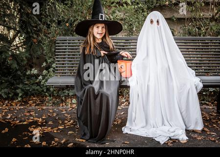 Young boy dressed in a bed sheet to be a ghost, and a young girl in witch costume holding a pumpkin pail for halloween. Stock Photo