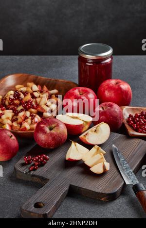 Still life with fresh lingonberries, red appples with knife on black cutting board and jar of homemade jam on dark background. Autumn harvest, Home ca Stock Photo