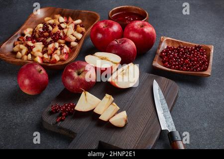 Still life with fresh lingonberries, red appples with knife on black cutting board and  homemade jam on wooden bowl on dark background. Top view. Autu Stock Photo