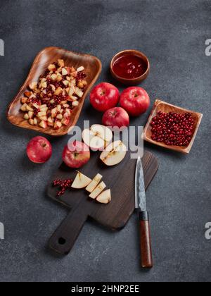 Still life with fresh lingonberries, red appples with knife on black cutting board and  homemade jam on wooden bowl on dark background. Top view. Autu Stock Photo
