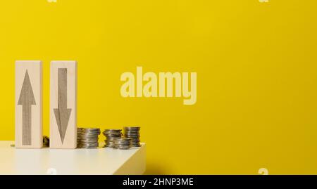 two wooden bars with arrows up and down on the table with coins, yellow background. Falls and increases in prices for utilities, exchange rates Stock Photo