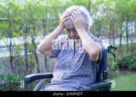 Asian senior or elderly old lady woman patient headache while sitting on bed in nursing hospital ward, healthy strong medical concept Stock Photo