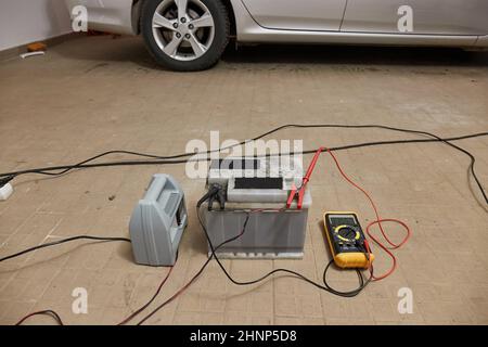 Charging a car starter battery, in a garage, monitoring state with digital multimeter Stock Photo