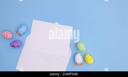 Paper card note in envelope with Easter eggs on bright pastel blue background. Creative copy space flat lay composition Stock Photo