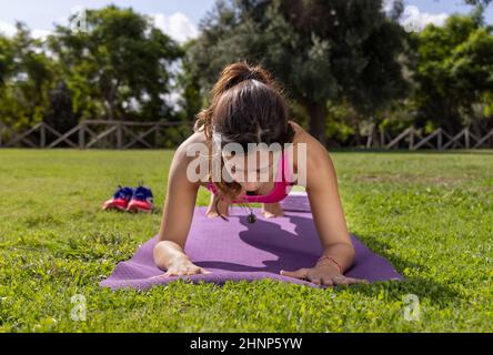 Young concentrated woman in plank position on mat in a park in a summer day Stock Photo