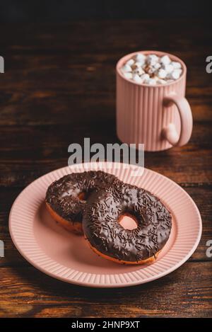 Two Chocolate Donuts and Mug of Hot Chocolate with Marshmallow on Rustic Wooden Surface Stock Photo