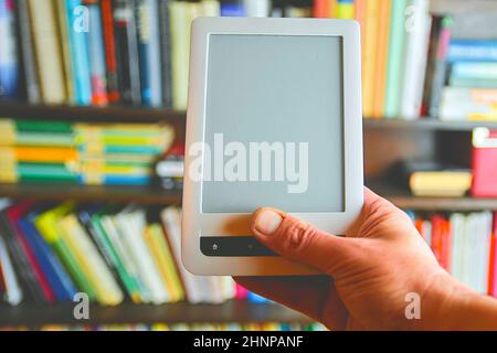 Ebook or digital reading tablet device. E-book in man's hand.  On the background is the shelf with bright real books. Online shopping books concept Stock Photo