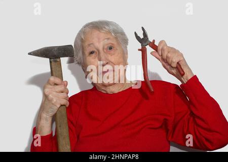 Funny portrait of senior woman holding hammer and pliers in his hand isolated on white Stock Photo