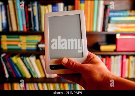 Ebook or digital reading tablet device. E-book in man's hand.  On the background is the shelf with bright real books. Online shopping books concept Stock Photo
