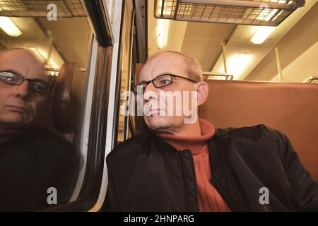 Middle age man looking out of the window of train. Passenger during travel by high speed express train in Europe. Elderly man travelling in train at night