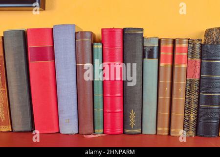 Wooden shelf with historic,decorated, vintage books. Old books on yellow and claret background Stock Photo