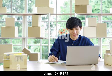 Young asian entrepreneur checking products stock at home office. Work from home concept. Stock Photo