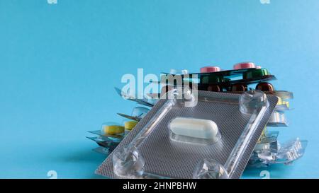 Packs of pills of various shapes and colors are stacked on a blue background. Capsules are packaged in blister packs. Different medicines. Drug treatment. Health photo. Copy space. Stock Photo