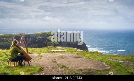 Woman playing harp on the top of iconic Cliffs of Moher, Ireland Stock Photo