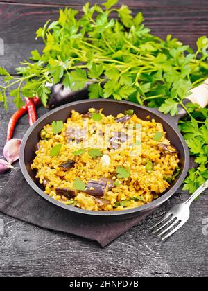 Bulgur stewed with eggplants, carrots, garlic and onions in a pan on a napkin on wooden board background Stock Photo