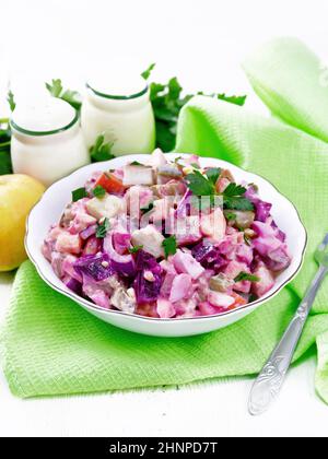 Finnish salad Rosoli of herring, beet, potatoes, pickles, carrots, onions and eggs, dressed with mayonnaise in a bowl on wooden board background Stock Photo