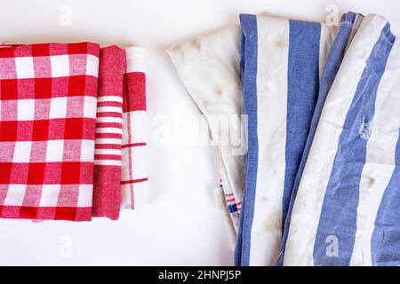 Three new red checkered kitchen picnic towels folded versus old dirty torn blue cloth towels. Cleaning and regularly changing kitchen rags and cloth. Stock Photo