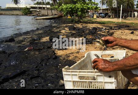 Fishermen collect the spilled crude this Thursday, February 17, 2022, on the shores of Lake Maracaibo in Venezuela. The Venezuelan hydrocarbon industry has for several years presented a series of operational problems due to the lack of maintenance of its facilities. This serious situation has caused spills of crude oil on land and sea, damaging agricultural and fishing areas, threatening marine life, the soil and finally the health of Venezuelans. In Venezuela there is no regulatory body that broadly establishes energy and environmental policy, nor does it force PDVSA to comply with regulation Stock Photo