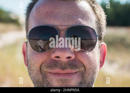 Bearded man making selfie with digital camera. Focus on camera reflected in sunglasses Stock Photo