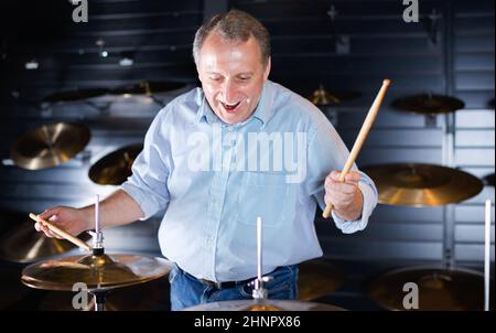 Musician male is choosing drum set and playing on it in music shop. Stock Photo