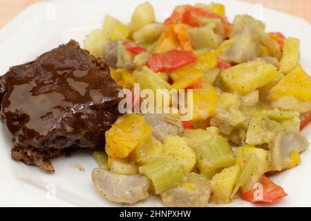 Cooked meatloaf with gravy and steamed potato in butter with black pepper on a plate. Savory meal of potatoes, celery and sweet peppers with butter an Stock Photo