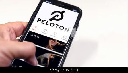A hand holding a phone with the Peloton app on the screen Stock Photo