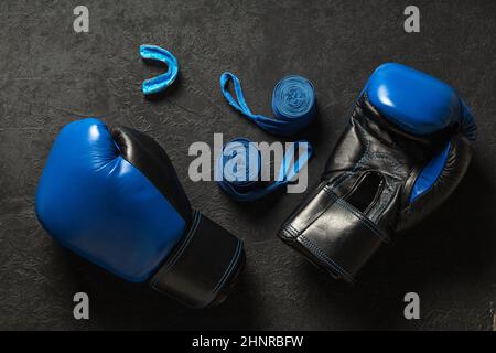 Boxing gloves with mouthguard and blue boxing bandages on a black background. Stock Photo