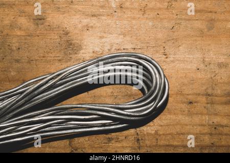 Grey wire on a wood background. wire without braiding lies on the wooden table. work tool Stock Photo