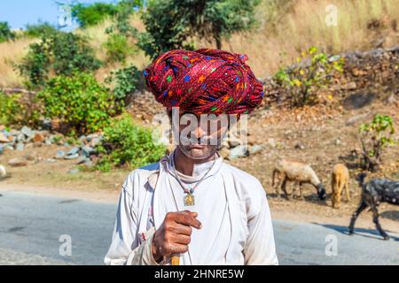 A Rajasthani tribal man wearing traditional colorful red turban and protects the goats Stock Photo