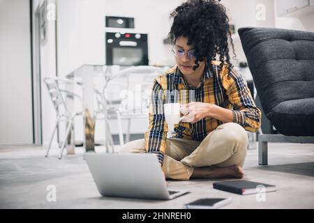 Afro woman working drinking coffee sitting on floor of her house Stock Photo