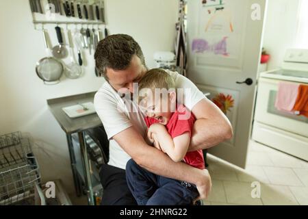High Angle View of Father Embracing Happy Son in Kitchen at Home Stock Photo