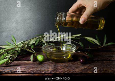Hand pouring olive oil on wooden table Stock Photo