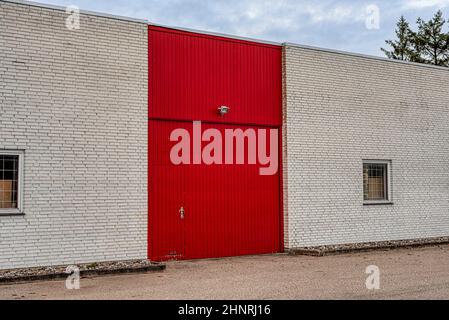 red door and gate on a white brick wall at the front of a storehouse with windows with grids, Frederikssund, Denmark, Februar, 17, 2022 Stock Photo