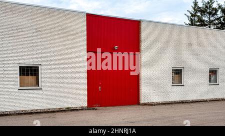 red door and gate gate on a white brick wall at the front of a storehouse with windows with grids, Frederikssund, Denmark, Februar, 17, 2022 Stock Photo