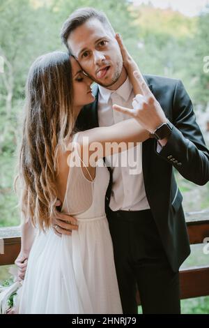Portrait of a bride touching the groom's face with sensuality and love as he shows the rock sign and tongue to the camera. The concept of facial Stock Photo