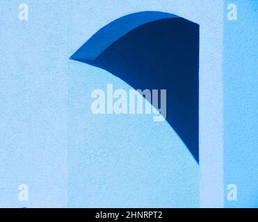 abstract design of shadow on blue concrete cement wall creating gemoetrical shapes in archway of exterior building triangular curved lines and angles Stock Photo