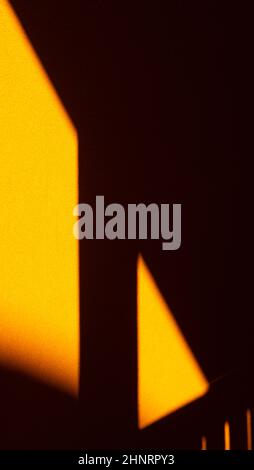 Shadow of staircase and railing cast onto yellow cement or concrete wall creating geometrical shapes rectangle and triangle with diagonal lines space Stock Photo