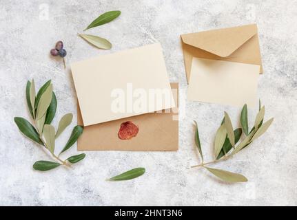 Wedding invitation cards and envelopes on a white marble table with olive branches top view. Elegant modern template with horizontal blank paper cards Stock Photo