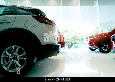 White luxury SUV car parked in modern showroom and blurred red car. Car dealership and auto leasing concept. Automotive industry. Showroom interior. New car stock for sale. Glass building of showroom. Stock Photo