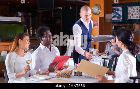 Polite waiter bringing ordered drinks to restaurant guests Stock Photo