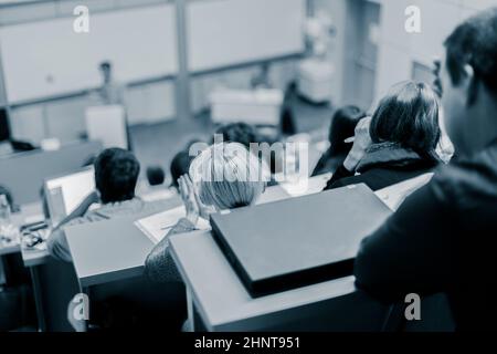 Speaker giving presentation in lecture hall at university. Participants listening to lecture and making notes. Stock Photo