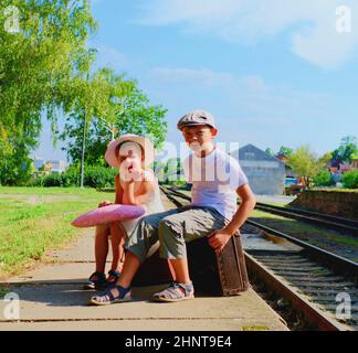 Adorable little girl and boy on a railway station, waiting for the train with vintage suitcases. Traveling, holiday and chilhood concept. Travel insurance concept Stock Photo