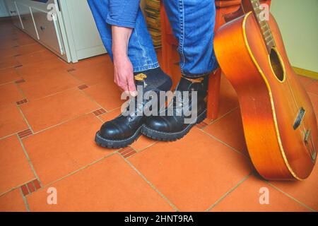 Rock and roll concept. Black boots and acoustic guitar. Putting on rock and roll boots Stock Photo